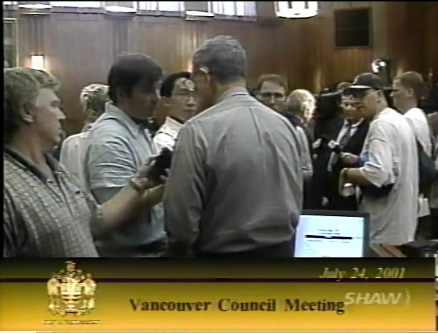 A screen capture showing reporters, including CBC’s Stephen Quinn in his municipal affairs reporter days, gathered around Councillor Bass in the Council chamber after demonstrators halt the July 24, 2001 meeting. Reference code: AM1487-F10-: 2020-040.01